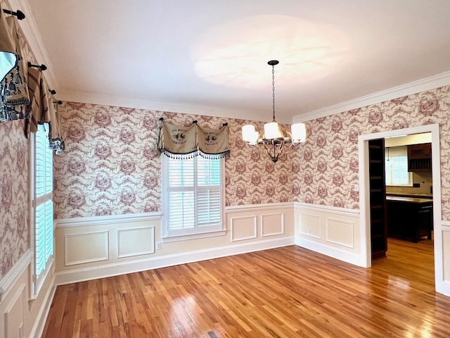 unfurnished dining area featuring crown molding, hardwood / wood-style floors, and a notable chandelier