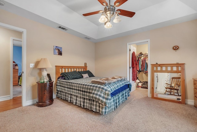 carpeted bedroom featuring a raised ceiling, a spacious closet, ceiling fan, and a closet