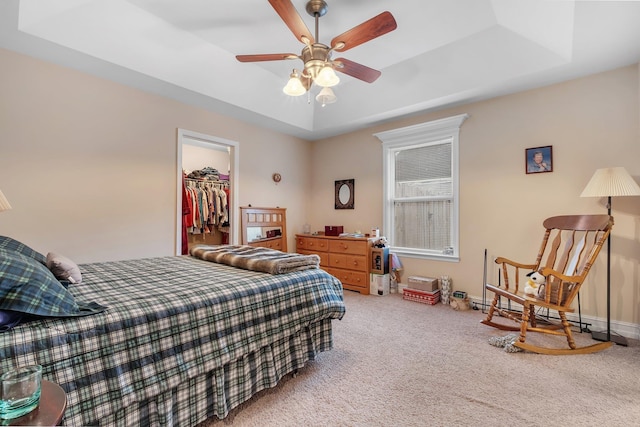 carpeted bedroom featuring a closet, a walk in closet, ceiling fan, and a tray ceiling