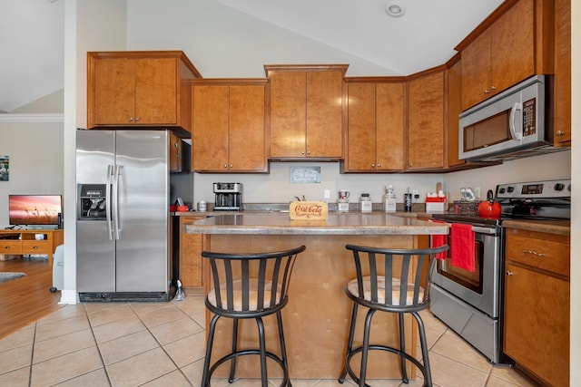 kitchen with lofted ceiling, appliances with stainless steel finishes, a center island, a kitchen bar, and light tile patterned flooring