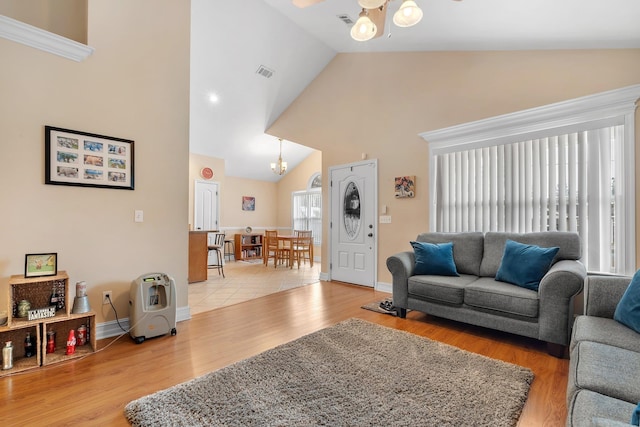 living room featuring ceiling fan with notable chandelier, high vaulted ceiling, and light wood-type flooring