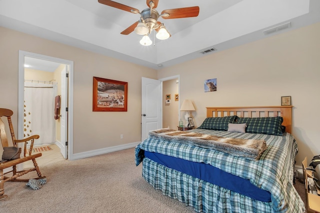 bedroom featuring light carpet, ensuite bath, a raised ceiling, and ceiling fan