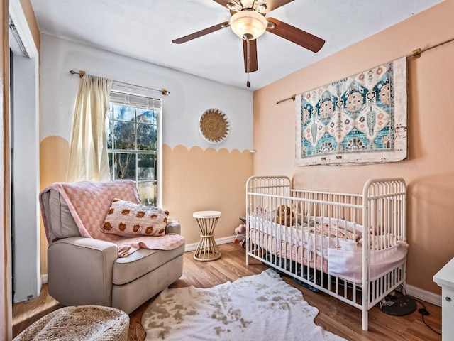 bedroom with hardwood / wood-style flooring, ceiling fan, and a crib