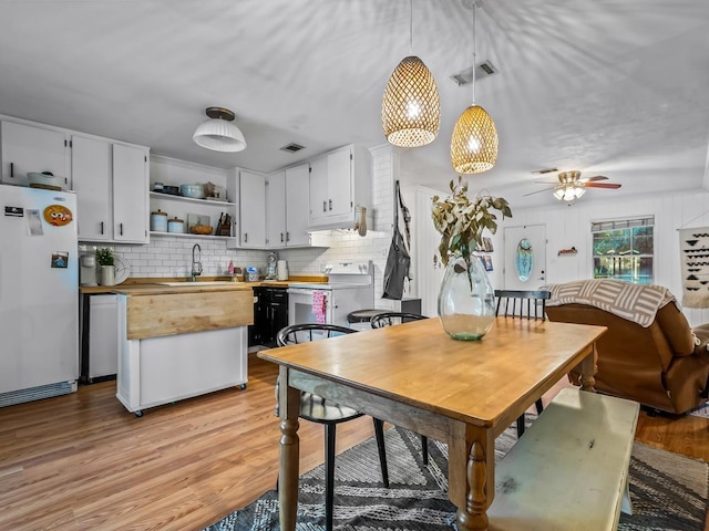 kitchen with sink, white appliances, wooden counters, hanging light fixtures, and white cabinets