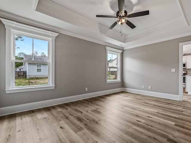 empty room with a raised ceiling, crown molding, ceiling fan, and light hardwood / wood-style flooring