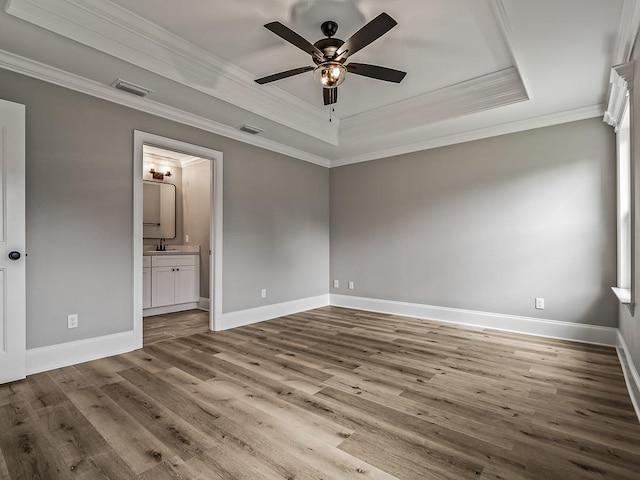 unfurnished bedroom with crown molding, connected bathroom, a tray ceiling, and ceiling fan