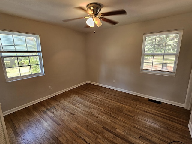 empty room featuring a ceiling fan, visible vents, dark wood finished floors, and baseboards