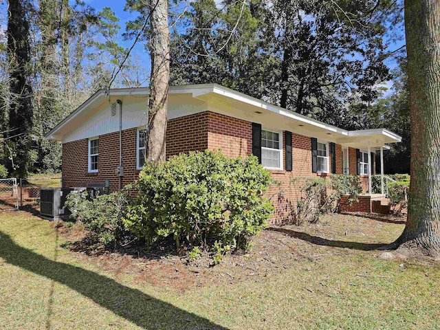 view of property exterior with brick siding, a yard, fence, and central air condition unit