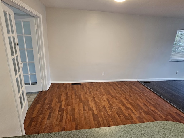 unfurnished room with dark wood-style floors, visible vents, and baseboards