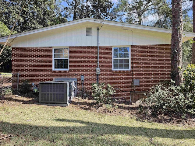 rear view of property with central air condition unit, a lawn, and brick siding