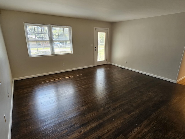 spare room featuring baseboards, dark wood-style flooring, and a healthy amount of sunlight