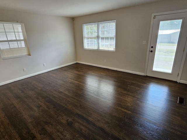 spare room featuring dark wood-type flooring, visible vents, and baseboards