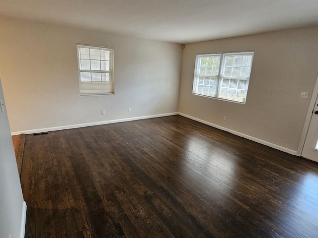 unfurnished room featuring dark wood-style flooring, visible vents, and baseboards