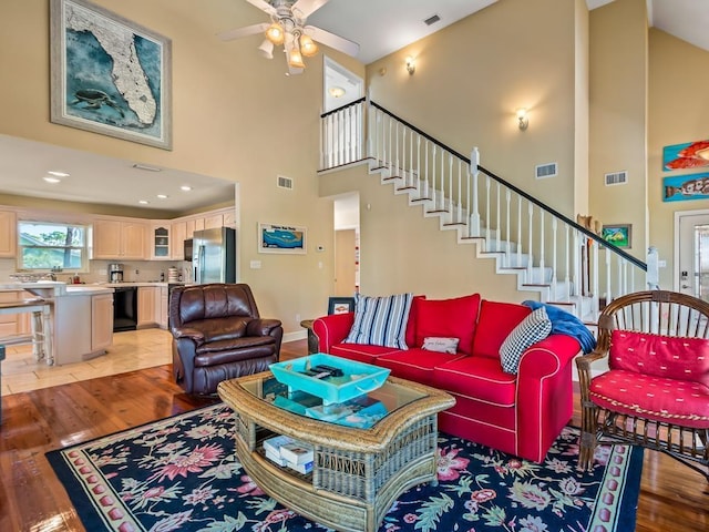 living room with ceiling fan, a high ceiling, and light wood-type flooring