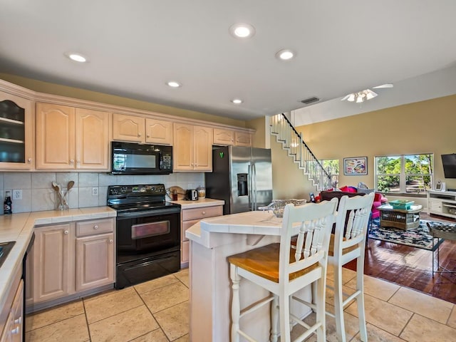 kitchen featuring tile counters, backsplash, a breakfast bar area, light tile patterned flooring, and black appliances