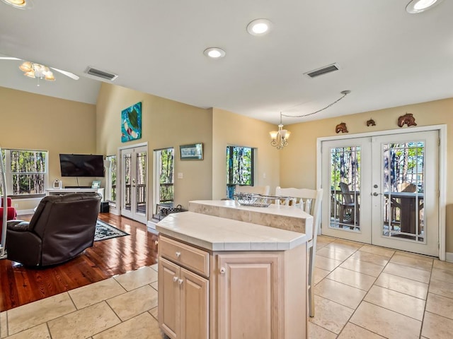 kitchen featuring french doors, a kitchen island, light tile patterned flooring, and ceiling fan with notable chandelier