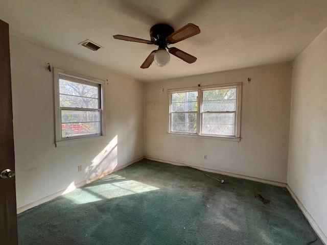 unfurnished room featuring ceiling fan, a wealth of natural light, and dark colored carpet