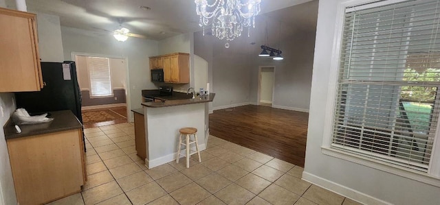 kitchen with black appliances, kitchen peninsula, a breakfast bar, ceiling fan with notable chandelier, and light hardwood / wood-style flooring