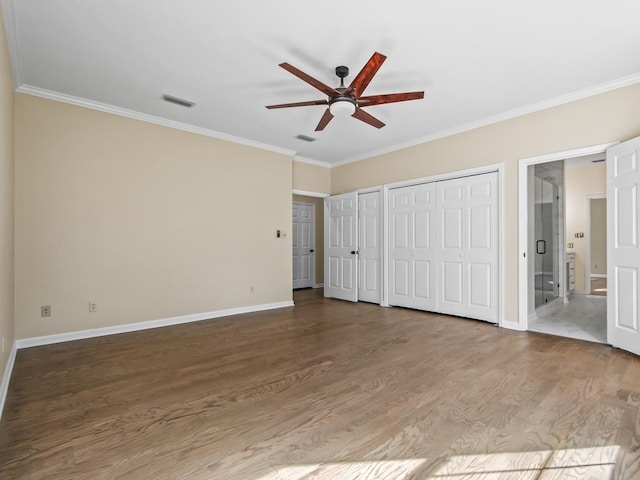 unfurnished bedroom with ornamental molding, wood-type flooring, two closets, and ceiling fan