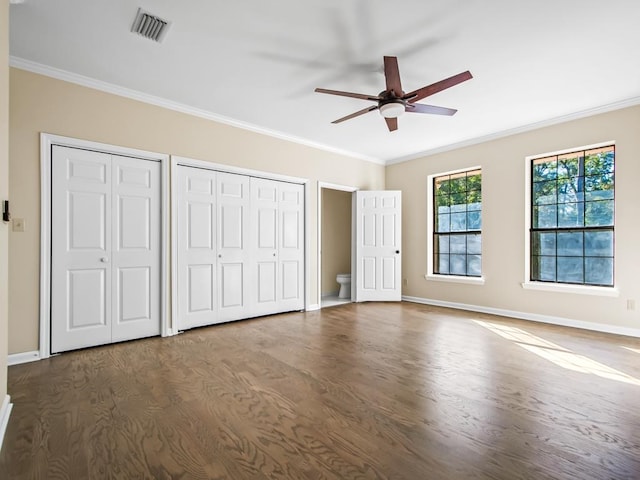 unfurnished bedroom featuring ceiling fan, multiple closets, dark hardwood / wood-style flooring, and ornamental molding