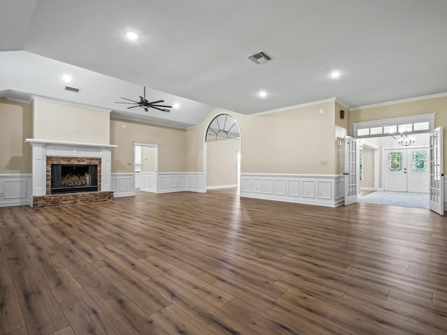 unfurnished living room featuring a brick fireplace, french doors, ceiling fan with notable chandelier, dark wood-type flooring, and crown molding