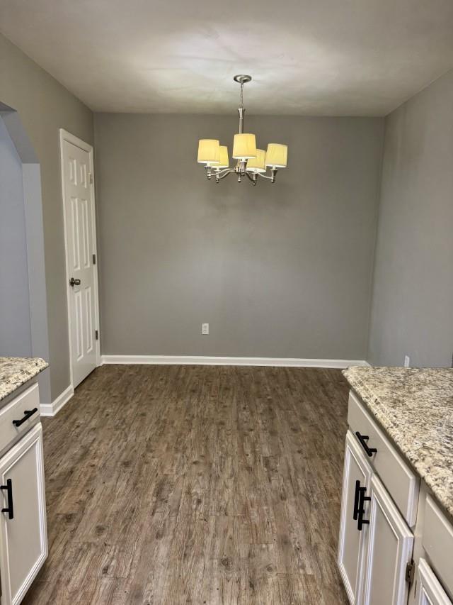 unfurnished dining area with a chandelier and dark wood-type flooring