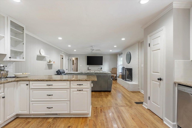 kitchen with a fireplace, white cabinetry, stainless steel dishwasher, ceiling fan, and light hardwood / wood-style floors