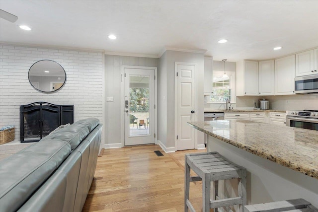 kitchen featuring pendant lighting, appliances with stainless steel finishes, a fireplace, light stone countertops, and light wood-type flooring