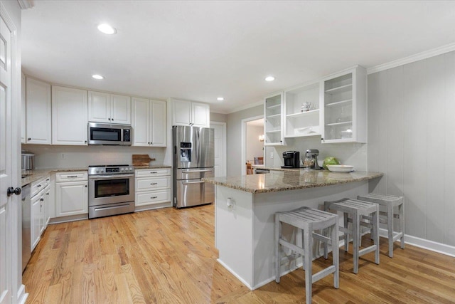 kitchen featuring light stone counters, light wood-type flooring, kitchen peninsula, stainless steel appliances, and white cabinets