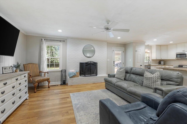 living room with sink, ceiling fan, crown molding, a brick fireplace, and light wood-type flooring