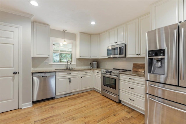 kitchen featuring sink, white cabinetry, stainless steel appliances, light stone counters, and decorative light fixtures