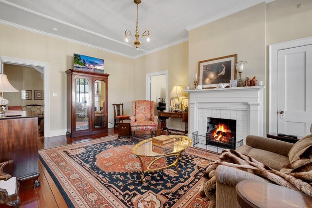 living room featuring a tiled fireplace, crown molding, dark hardwood / wood-style floors, and an inviting chandelier