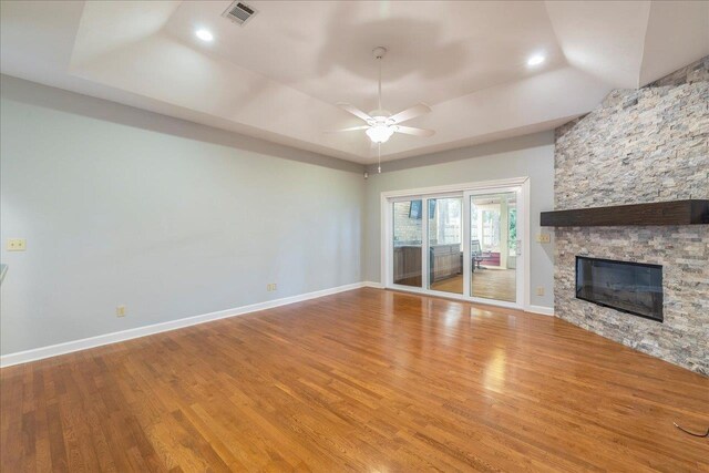 unfurnished living room featuring a tray ceiling, visible vents, a stone fireplace, wood finished floors, and baseboards