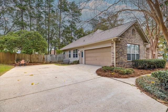 view of property exterior featuring brick siding, a shingled roof, fence, a garage, and driveway