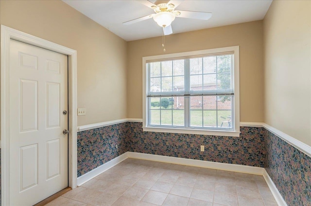 empty room with a ceiling fan, light tile patterned flooring, wainscoting, baseboards, and wallpapered walls