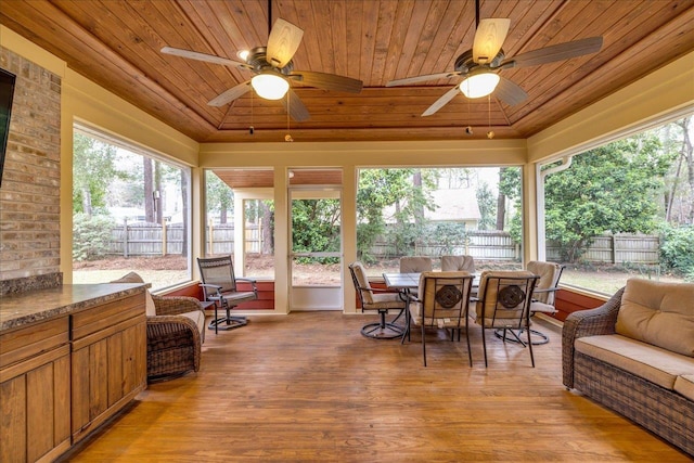 sunroom with ceiling fan, wooden ceiling, a raised ceiling, and a healthy amount of sunlight