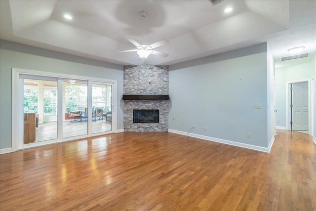 unfurnished living room with baseboards, visible vents, wood finished floors, a tray ceiling, and a stone fireplace