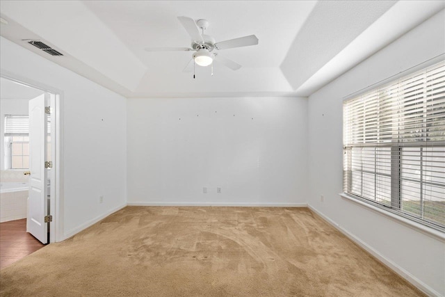 empty room featuring light colored carpet, ceiling fan, and a raised ceiling