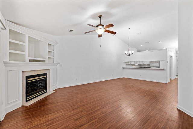 unfurnished living room featuring built in shelves, a fireplace, vaulted ceiling, hardwood / wood-style flooring, and ceiling fan with notable chandelier