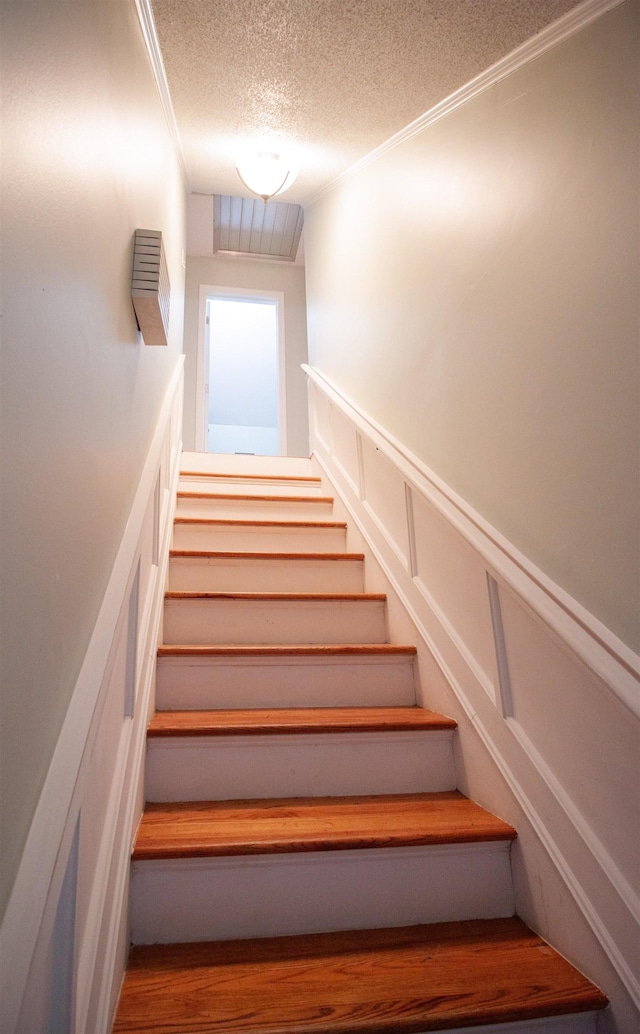 staircase with wainscoting, crown molding, a decorative wall, and a textured ceiling