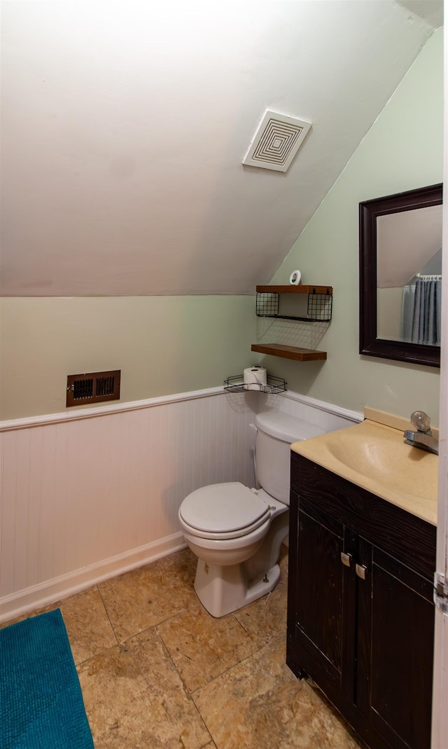 bathroom featuring vanity, vaulted ceiling, toilet, visible vents, and wainscoting