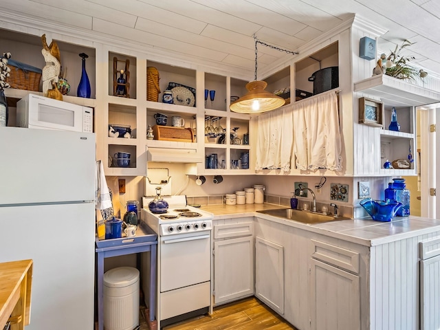 kitchen with sink, stainless steel counters, hanging light fixtures, white appliances, and light wood-type flooring