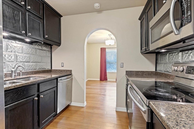 kitchen featuring appliances with stainless steel finishes, light hardwood / wood-style floors, dark stone countertops, and sink