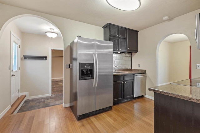 kitchen with appliances with stainless steel finishes, backsplash, light hardwood / wood-style floors, and sink