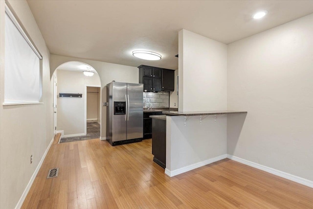 kitchen with a breakfast bar, sink, stainless steel refrigerator with ice dispenser, light hardwood / wood-style flooring, and kitchen peninsula