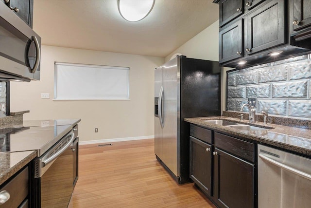 kitchen with stainless steel appliances, light hardwood / wood-style flooring, dark stone countertops, and sink