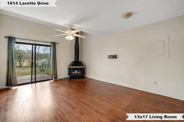 unfurnished living room with a wood stove, electric panel, baseboards, and wood finished floors