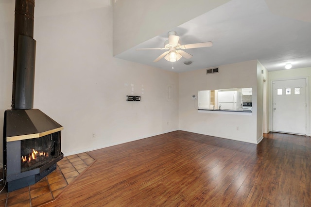 unfurnished living room featuring dark wood finished floors, visible vents, a ceiling fan, a wood stove, and baseboards