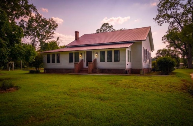 view of front facade featuring entry steps, a chimney, metal roof, and a front yard