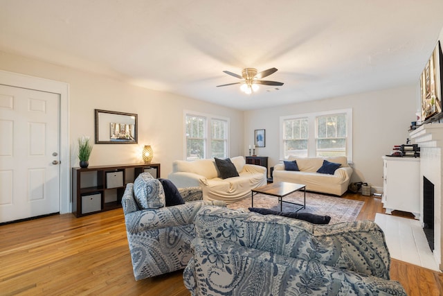 living room featuring ceiling fan, a fireplace, and light wood-type flooring